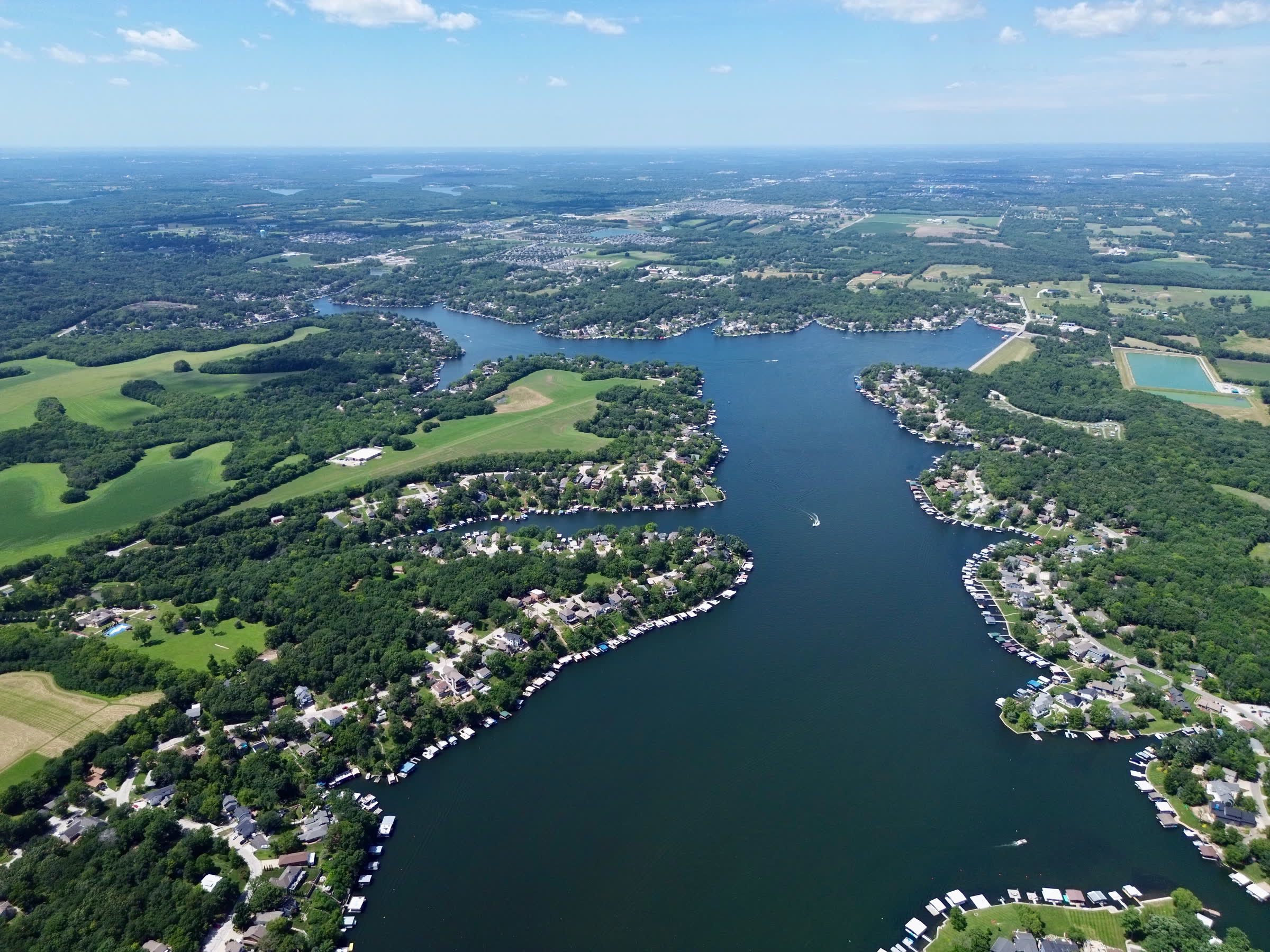 Aerial view of Lake Lotawana with tree-lined shorelines, coves, and docks reaching into calm blue water